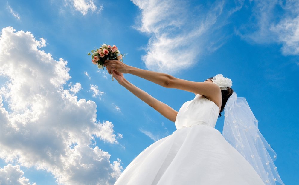 Bride in a white gown holding a bouquet up against a blue sky