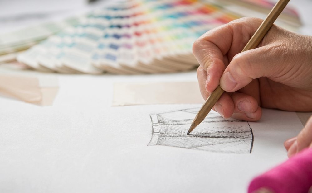 Hand sketching a garment design beside a fan of colour swatches